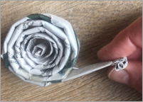 A hand holding a coiled piece of newspaper and making the snail's head. Background is a wooden table. 