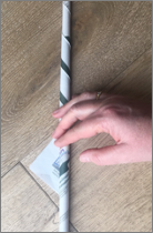 A hand rolling a newspaper into a tight tube on a wooden table.