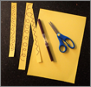 A piece of yellow card cut into strips. The strips are decorated on one side.
